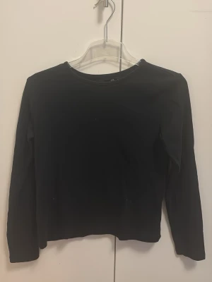 Svart långärmad basic tröja - En enkel svart långärmad tröja med rund halsringning. Modellen är rak och har en tight passform, perfekt att matcha med jeans eller kjol. Tillverkad i mjukt och stretchigt material för skön känsla hela dagen.