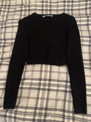 Svart croppad långärmad topp - En svart croppad topp med långa ärmar och rund hals. Enkel och stilren design som passar perfekt till höga jeans eller kjol. Materialet känns mjukt och relativt stretchigt för en bekväm passform.