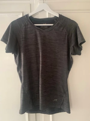 Mörkgrå träningströja från Pro Touch - Tillverkad i ett lätt och snabbtorkande material som passar perfekt för träning och aktivitet. Kortärmad modell med bekväm passform. I jättefint skick. 