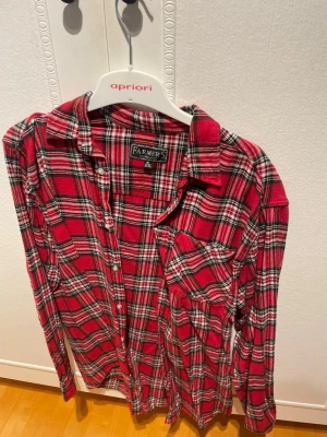 Röd rutig skjorta från Farmer's - Klassisk röd rutig skjorta från Farmer's i mjuk bomull. Skjortan har långa ärmar, bröstficka och knappar framtill. Perfekt för en avslappnad och cool stil. Passar dig som gillar tidlös design och bekväma material.