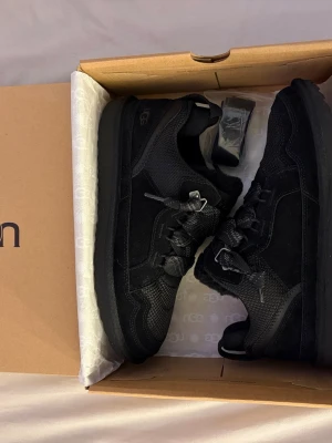 Svarta UGG sneakers i mesh och mocka - Snygga helsvarta sneakers från UGG med en mix av mesh och mocka på ovandelen. Skorna har breda svarta skosnören, diskret UGG-logga på sidan och en tjock sula för extra komfort. Perfekta för dig som gillar en stilren och sportig look.