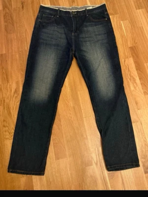 Mörkblå Wrangler jeans med raka ben - Säljer ett par mörkblå jeans från Wrangler med raka ben och klassisk femficksmodell. Jeansen har snygga slitningar framtill och bakfickor med broderade detaljer. Tillverkade i kraftig denim som ger en cool och tidlös look.