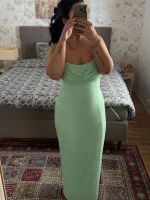 Mintgrön axelbandslös långklänning OH POLLY - Säljer en mintgrön axelbandslös långklänning med draperad överdel. Klänningen har en figurnära passform och är perfekt för dig som vill sticka ut med en fräsch färg. Materialet känns mjukt och stretchigt.