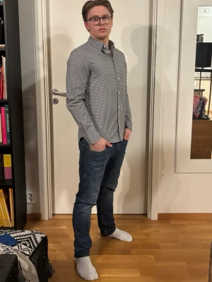 Gråvitrutig Ralph Lauren skjorta med klassisk krage - Stilren skjorta i grått och vitt rutmönster med klassisk krage och knäppning framtill. Långärmad modell som passar perfekt till jeans eller chinos. Skjortan har en smal passform och är tillverkad i ett mjukt bomullstyg.