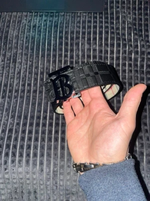 Svart Burberry bälte med TB-spänne - Snyggt svart bälte från Burberry med klassiskt rutmönster och stort TB-spänne i metall. Bältet är gjort i skinn och har en exklusiv känsla med detaljer som sticker ut. Perfekt accessoar för att lyfta din outfit.