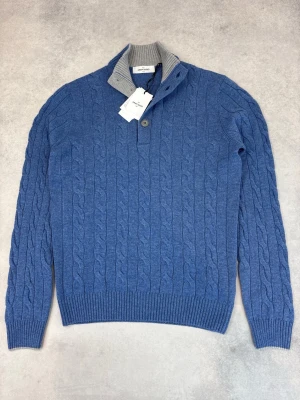 Blå kabelstickad tröja Gran Sasso - Snygg blå kabelstickad tröja från Gran Sasso med ribbstickad grå krage och knappslå. Tröjan har långa ärmar, ribbade muddar och klassisk kabelstickad struktur. Perfekt för dig som gillar stilren och tidlös design.