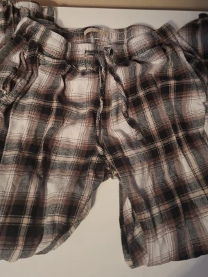 Rutiga pyjamasshorts från 157 - Mysiga pyjamasshorts från 157 i brun, svart och vit rutig design. Shortsen har resårmidja med dragsko för skön passform och är tillverkade i mjukt, tunt tyg som passar perfekt för chillkvällar hemma. För både kvinnor och män