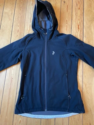 Svart jacka Peak Performance - Svart snygg vindjacka från Peak Performance med huva och dragkedja. Jackan har två sidofickor med dragkedja. Tillverkad i ett mjukt, vindtätt material som passar perfekt för blåsiga dagar!!😍😍