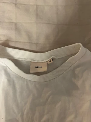 Vit omlottopp med knyt från Nelly - Säljer en vit omlottopp från Nelly i storlek XS. Toppen har korta ärmar och ett snyggt knyt i midjan som ger en trendig look. Perfekt att styla med jeans eller kjol för en fräsch outfit.