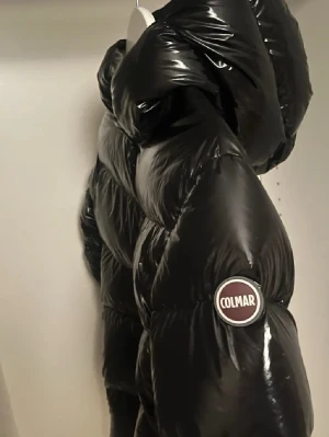 Svart glansig dunjacka från Colmar - Snygg svart dunjacka från Colmar med glansig finish och stor huva. Jackan har en tydlig logotyp på ärmen och är perfekt för kalla vinterdagar. Klassisk puffer-modell som håller värmen och ger en cool look. 16 år, 172cm alltså Xs-S.                Knappt använd      NYRPIS: 5000kr säljer billigt för vill ha sålt 