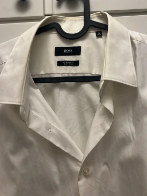 Vit skjorta från BOSS Regular Fit - Klassisk vit skjorta från BOSS i Regular Fit med enkel krage och knappar framtill. Skjortan är tillverkad i bomull och har lång ärm. Perfekt för en clean och stilren look.