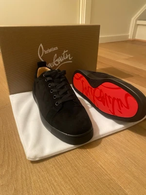 Svarta sneakers från Christian Louboutin - Säljer ett par svarta sneakers från Christian Louboutin i mocka med klassisk röd sula och svarta skosnören. Skorna har en stilren och lyxig design med låg profil och diskreta detaljer. Perfekta för dig som vill ha något exklusivt och trendigt.
