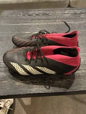 Adidas Predator fotbollsskor svart/rosa - Säljer ett par Adidas Predator fotbollsskor i svart och rosa med vita detaljer. Skorna har en strumpliknande passform, snörning och mönstrad ovandel för bättre bollkontroll. Ikoniska tre ränder på sidan och texten 'Predator' tryckt på skon. Inte super skick på dessa därav priset… Köptes för 2799kr säljer dom nu för 500kr