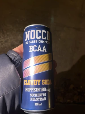 Nocco BCAA Cloudy Soda 330 ml - En blå burk Nocco BCAA Cloudy Soda, 330 ml. Drycken är sockerfri, kolsyrad och innehåller 180 mg koffein. Burken har färgglada detaljer i gult och rosa samt tydlig text på framsidan.