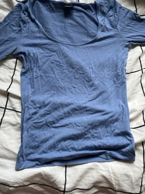 Ljusblå enkel topp med rund hals - En basic ljusblå topp med rundad halsringning och långa ärmar. Tillverkad i mjukt bomullsmaterial som känns skönt mot huden. Perfekt att styla lager på lager eller bära som den är. Enkel och stilren design utan mönster eller detaljer.