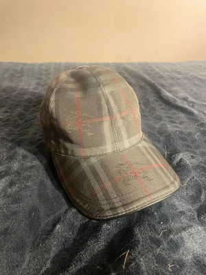 Svart burberry keps med justerbart band - Säljer en stilren burberry keps. Kepsen har böjd skärm och justerbart band bak i metall. 