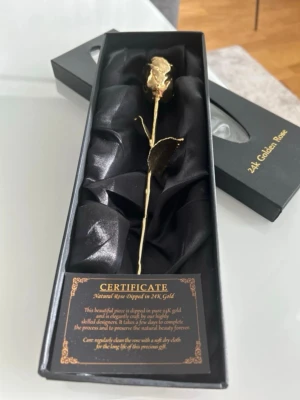 24K guldpläterad ros i presentask - Unik ros doppad i 24K guld, levereras i en elegant svart presentask med certifikat. Rosens form är naturtrogen med detaljerade blad och stjälk, vilket gör den till en lyxig och dekorativ accessoar eller samlarobjekt. Perfekt som exklusiv gåva eller dekoration.