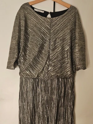 Glittrig metallic minidress med v-ringning - Säljer en snygg minidress i metallic silver med glittrig finish. Den har korta ärmar, v-ringning och plisserad struktur. Materialet är stretchigt och skimrande, perfekt för dig som vill sticka ut. Från Mango