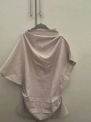 Ljusbeige vid blus med kort ärm - Trendig ljusbeige blus med lös passform och breda korta ärmar. Blusen har en hög halsringning och dragkedja i ryggen. Tillverkad i ett slätt, vävt tyg som ger en stilren look. Perfekt för dig som gillar minimalistisk och modern stil. För fler bilder/information skriv gärna, priset kan justeras 🤗❤️