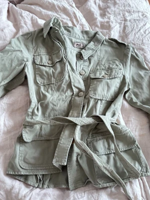 Khakigrön safarijacka - Trekvartsärmad jacka i khaki grön färg med knytband runt midjan
