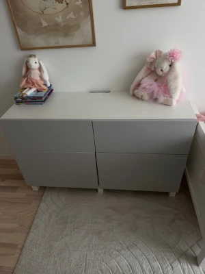 Vit och grå förvaringsmöbel - Säljer en stilren förvaringsmöbel i vitt och ljusgrått med fyra lådor. Perfekt för att organisera saker i sovrum eller barnrum. Möbeln har raka linjer och står på små ben vilket ger ett modernt intryck.