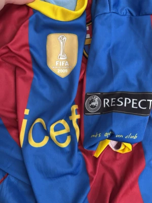 FC Barcelona Ronaldinho tröja #10 - Säljer en klassisk FC Barcelona matchtröja med Ronaldinho och nummer 10 på ryggen. Tröjan är blå och röd med gula detaljer, FIFA World Champions 2009-märke och UEFA Respect-märke på ärmen. Materialet är lätt och andas, perfekt för fotboll eller samling.