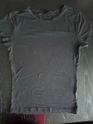 Svart t-shirt från Gina Tricot - En enkel svart t-shirt från Gina Tricot i mjukt bomullsmaterial. Modellen är klassisk med rund halsringning och korta ärmar. Perfekt basplagg att matcha med allt och har en slim fit passform🌸