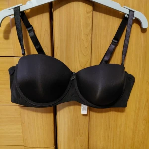Svart push-up bh med avtagbara band - Svart axelbandslös BH med avtagbara axelband. BH:n har formpressade kupor och en liten rosett framtill. Knäppning baktill med hakar och hyskor. Storlek 85D, Oanvända.