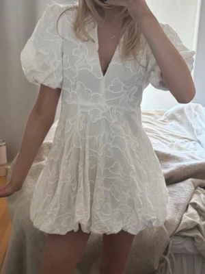  Ny student Vit kortklänning med puffärm - Supersöt vit kortklänning med puffärmar och v-ringning. Klänningen har broderade blommönster och en lätt volangig kjol. Perfekt för sommarens alla tillfällen och ger en romantisk vibe.
