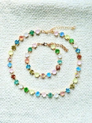 Färgglatt smyckespaket med stenar  - Säljer ett halsband och armband med gnistrande runda stenar i flera färger som blått, grönt, rosa, gult, vitt, aprikos, lila mm. Stenarna sitter i guldfärgade, reglerbara infattningar och ger ett lyxigt och lekfullt intryck. Perfekt för dig som vill sticka ut med färg och glans! Levereras i ask med satinband. 