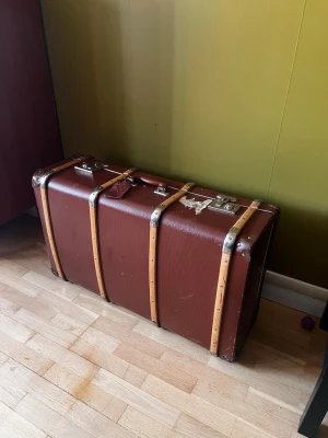 Vintage brun resväska med trädetaljer - Snygg gammaldags resväska i mörkbrunt med trädetaljer och metallbeslag. Klassisk rektangulär form och robust design, perfekt för dig som gillar retrostil. Väskan har handtag upptill och detaljer i silverfärgad metall.