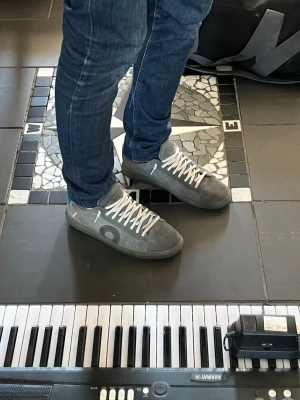 Gråa sneakers från Oliver cabell  - Snygga gråa sneakers från Oliver cabell med grå sula och vita skosnören. Skorna har en låg profil och är tillverkade i mocka med diskreta detaljer och logga på sidan. Perfekta för en stilren och avslappnad look.