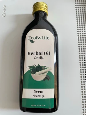 EcoByLife Neem Örtolja 150ml - Neem örtolja från EcoByLife i en mörk glasflaska med guldfärgat skruvlock. Innehåller 150 ml neemolja, perfekt för hud- och hårvård. Flaskan har en grön och vit etikett med bild på mortel och blad.
