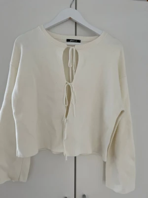 Vit stickad tröja med knytning - Trendig vit stickad tröja från Gina Tricot med tre knytband framtill. Tröjan har rund halsringning, långa ärmar och en avslappnad passform. Perfekt för lager-på-lager och att styla med jeans eller kjol. Storlek M