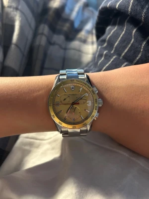 Victorinox silver/guld kronografklocka kan byta mot saker - Snygg kronografklocka från Victorinox med silverfärgad länk i metall och guldfärgad urtavla. Klockan har tachymeter, datumvisning och flera små urtavlor. Perfekt accessoar för dig som gillar stilrena detaljer och klassisk design.