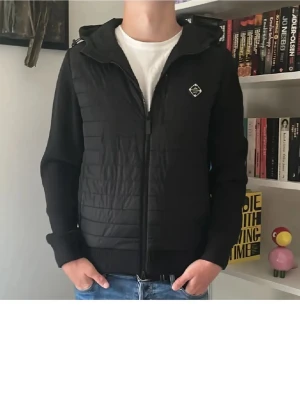 J Lindberg cardigan - Snygg svart cardiganjacka med quiltad front och stickade ärmar. Jackan har dragkedja, huva och en liten logotyp på bröstet. Perfekt för lager-på-lager den är är fin skick storlek S om intresse skriv elle mer bilder