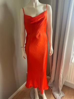 Orange långklänning med tunna band strl 40 - Snygg orange långklänning med tunna reglerbara axelband och lätt draperad urringning. En snygg djup urringning baktill .Klänningen har en slank passform och är tillverkad i ett glansigt material som ger en lyxig känsla. Perfekt för dig som vill sticka ut med färg och stil. Prislapp ej kvar i men helt ny aldrig använd 