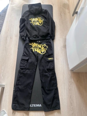 Minus Two dress - Cool svart hoodie med stor huva och fett gult graffiti-tryck på bröstet. Hoodien har ribbade muddar och är gjord i mjukt material, perfekt för streetwear-stilen. Passar dig som gillar att sticka ut med grafiska prints och urban vibe.
