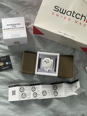 Omega x Swatch Moonshine Gold - Omega x Swatch MoonSwatch Mission to Earthphase – Moonshine Gold säljes i helt nytt och oanvänt skick. Klockan har aldrig använts och är i perfekt skick utan repor eller märken.  Skick: Ny / oanvänd Tillbehör: Box, papper och allt medföljer Frakt: Skickas snabbt och säkert  DM:a gärna vid frågor eller om du vill ha fler bilder.