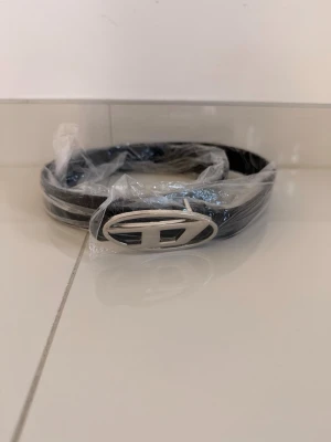 Diesel bälte – oanvänt i förpackning 🖤 - Säljer detta snygga Diesel-bälte med den ikoniska oval D-spännet i silver. Bältet är helt oanvänt och fortfarande i sin originalplast – perfekt skick!  ✔️ Märke: Diesel ✔️ Färg: Svart med silverspänne ✔️ Skick: Nytt, oanvänt ✔️ Nypris: ca 1 200–1 500 kr  Pris: 700 kr – kan diskuteras något!  📦 Frakt tillkommer. Snabb affär! 🙌
