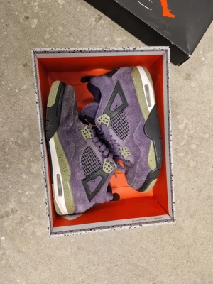 Air Jordan 4 Retro Purple Suede - Grymma Air Jordan 4 Retro sneakers i lila mocka med svarta och gröna detaljer. Klassisk siluett med meshpaneler, synlig Air-sula och Jumpman-logga på plösen. Perfekta för dig som vill sticka ut med stilrena och unika sneakers.