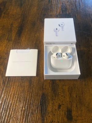 Apple AirPods 4 - Trådlösa vita Apple AirPods med laddningsetui. Snygg och minimalistisk design i plast, perfekt för dig som vill ha smidiga hörlurar till mobilen. Kommer i originalförpackning med tillhörande manual. Har även ljud brusreducering. Jag har testat så att hörlurar är smidiga och funkar bra