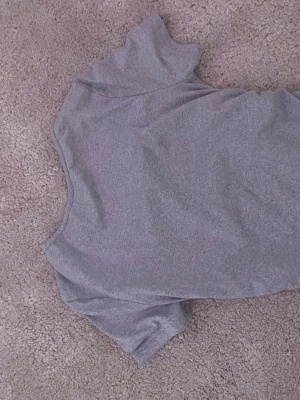 Grå basic t-shirt med rund hals - En enkel och stilren grå t-shirt med rund halsringning och korta ärmar. Perfekt att matcha med jeans eller kjol för en clean look. Tillverkad i mjuk bomull som känns skön mot huden.