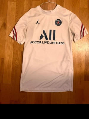 Vit PSG matchtröja Jordan - Säljer en vit PSG matchtröja från samarbetet med Jordan. Tröjan har blå och röda detaljer på ärmarna, PSG-logga på bröstet och texten 'Accor Live Limitless' framtill. Tillverkad i lätt och ventilerande material, perfekt för fotboll eller träning. Använt typ 3 gånger, självklart äkta, org pris 1200. Priset går att diskuteras!!!