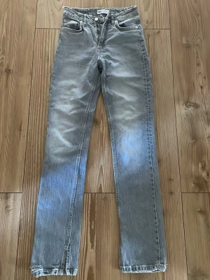 Grå raka jeans från Zara - Säljer ett par grå raka jeans från Zara med hög midja och klassisk femficksdesign. Jeansen har en tvättad look och är tillverkade i denim med en något vintage känsla. Perfekta för en avslappnad och trendig stil.