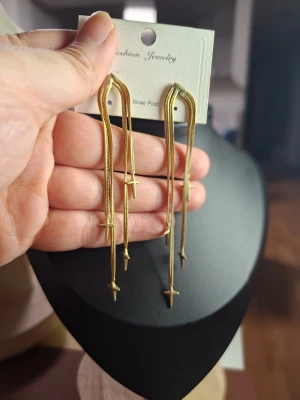 Guldiga långa örhängen med stjärnor - Säljer ett par trendiga örhängen i guldton med långa, tunna kedjor och små stjärndetaljer. Örhängena har en modern design och är lätta att matcha med olika stilar. Perfekta för dig som gillar statement-smycken och vill sticka ut.