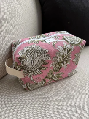 Rosa necessär med annansmöster - Necessär i tyg från Enkel med rosa botten och grönt/vitt (guld) mönster. Rektangulär form med dragkedja upptill och en beige bärrem på sidan. Perfekt för smink eller småprylar. Tygmaterial med stabil känsla och snygg design. Innertyg i beige med innerfack. Mått ca 27x17x12cm