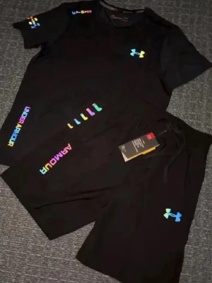  Under Armour - Snyggt svart träningsset från Under Armour med färgglada loggor och detaljer. Setet består av en t-shirt och shorts, båda med UA-loggan i regnbågsfärger. Perfekt för gymmet eller löprundan. Materialet är lätt och andas bra.