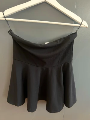 Svart bandeau topp från H&M Divided - Svart bandeau topp från H&M Divided med tunna axelband och lös, flowy passform. Toppen har en snygg draperad halsringning och är tillverkad i ett mjukt material som känns bekvämt mot huden. Perfekt för en trendig och avslappnad stil.