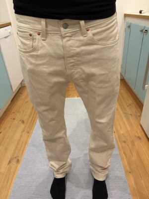 Vita raka jeans från Levi's - Säljer ett par vita jeans från Levi's med klassisk rak passform och fem fickor. Jeansen har silverfärgad knapp, nitar och Levi's röda logga på bakfickan. Tillverkade i kraftig denim med bälteshällor och normal midja. W31 L32. Perfekta vita jeans för sommaren. 1250 kr nya, är i helt nytt skicka använda någon timme men sen så har dom legat i gaderåben i 4 månader. Kan gå ner i pris vid snabb affär 